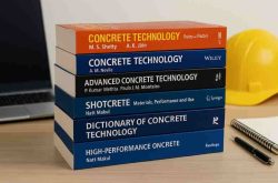 Stack of modern concrete technology and civil engineering textbooks on a desk with a laptop, notebook, pen, and construction helmet in the background.