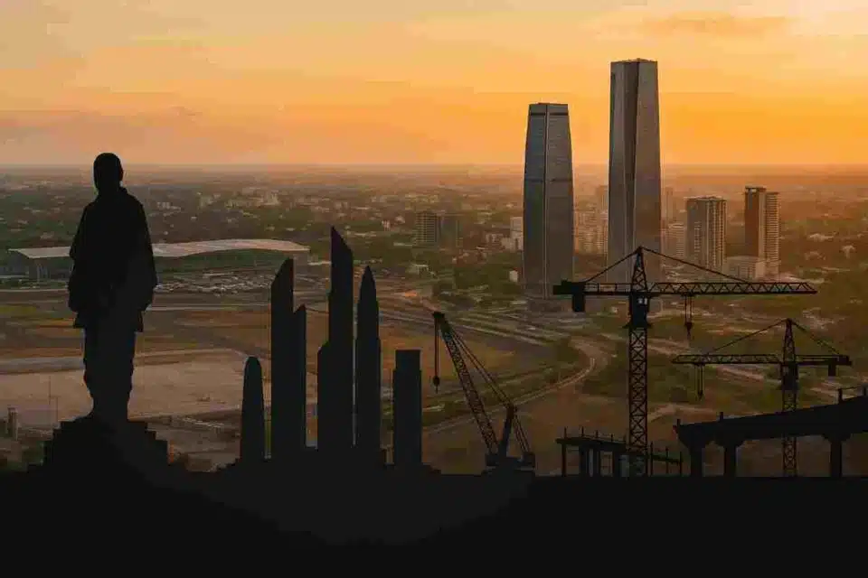 Panoramic aerial view of Gujarat’s skyline with silhouettes of the Statue of Unity, Dholera Smart City towers, and construction cranes at sunset.