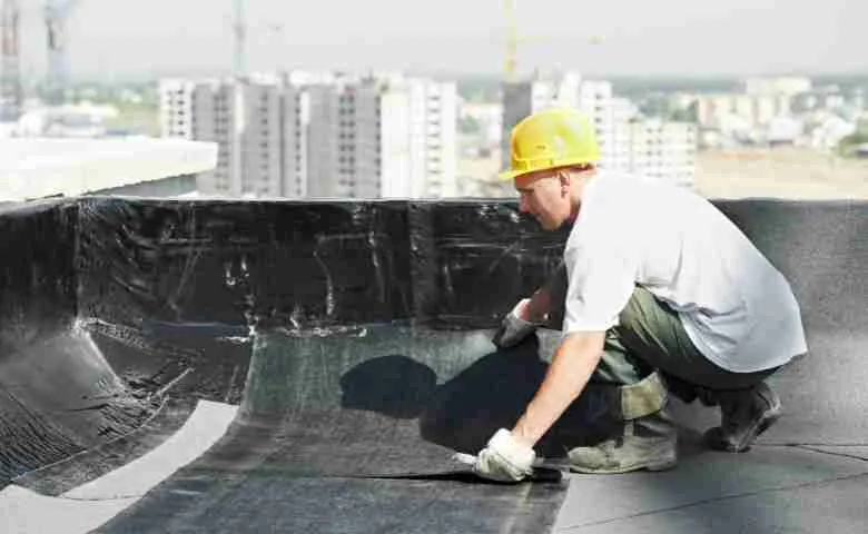 A team of construction workers installing an eco-friendly green roof on a modern building, with solar panels visible in the background.