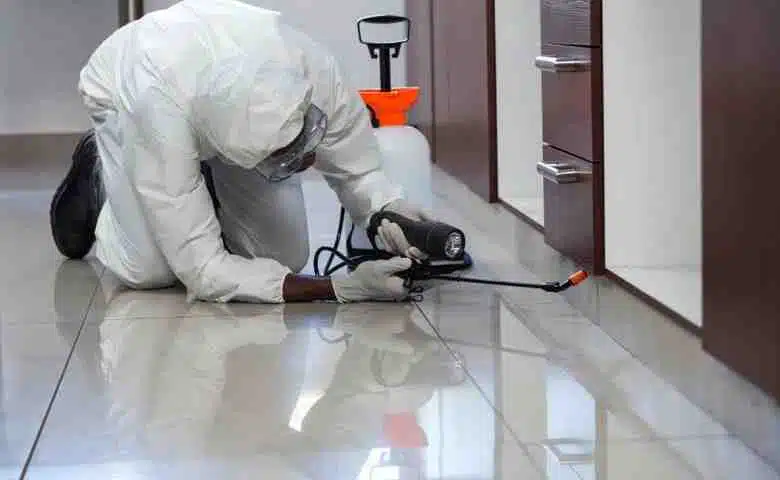 Technician applying pest control spray in a modern home while wearing full protective gear.