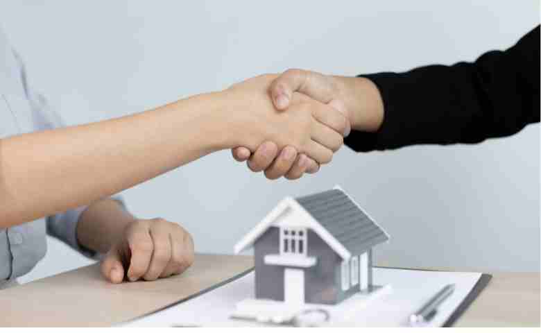 A handshake between two business professionals over a blueprint, symbolizing a real estate joint venture in India.