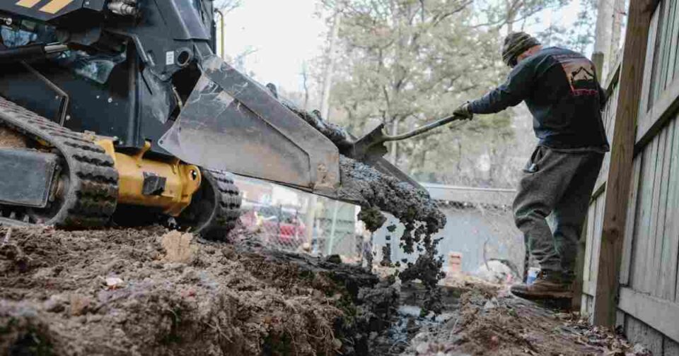 Skid steer fitted with a bucket beside auger and fork attachments on an active construction site